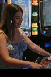 a-young-hispanic-woman-smiles-while-playing-slot-machines-in-a-casino-radiating-joy-and-the-thrill-of-gambling-2X7GXGN
